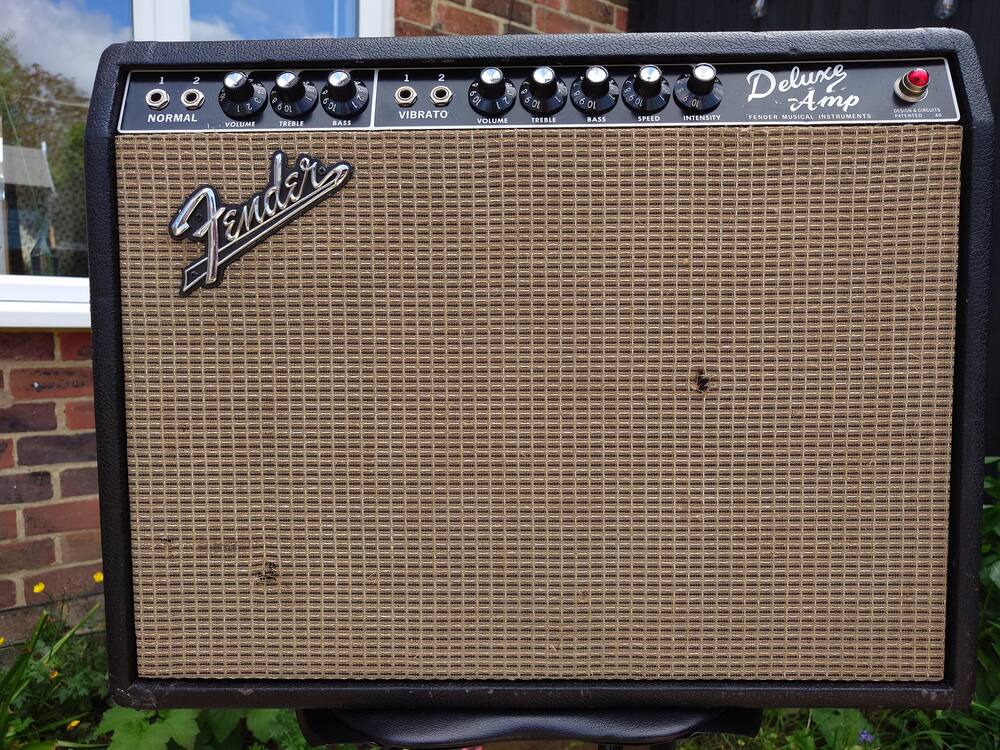 The Fender Deluxe from the front against a brick wall, the Fender logo and the Deluxe Amp badge on the grille cloth